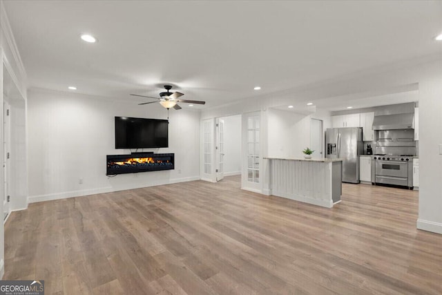 unfurnished living room featuring ceiling fan, light wood-type flooring, crown molding, and french doors