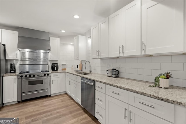 kitchen with sink, wall chimney exhaust hood, white cabinetry, appliances with stainless steel finishes, and light wood-type flooring