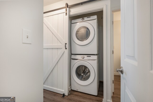 laundry area with stacked washing maching and dryer, dark hardwood / wood-style floors, and a barn door