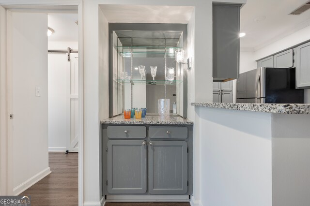 kitchen with light stone countertops, a barn door, dark hardwood / wood-style flooring, stainless steel fridge, and gray cabinets