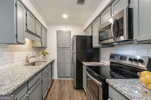 kitchen featuring appliances with stainless steel finishes, sink, gray cabinets, ornamental molding, and light hardwood / wood-style flooring