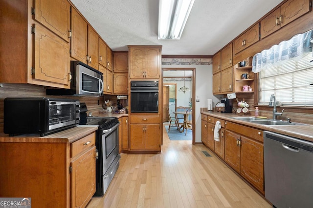 kitchen with sink, crown molding, light hardwood / wood-style flooring, appliances with stainless steel finishes, and a textured ceiling