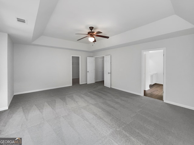 unfurnished bedroom with a spacious closet, ceiling fan, a tray ceiling, and dark carpet