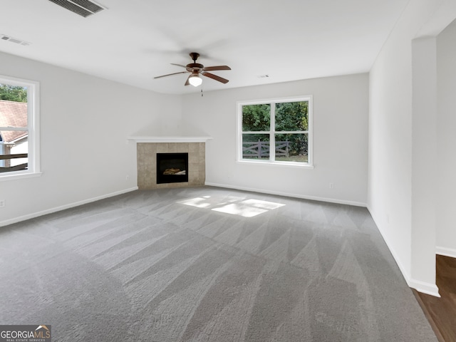 unfurnished living room with a tile fireplace, dark colored carpet, and ceiling fan