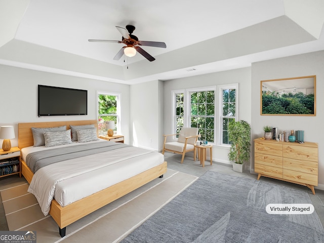 bedroom featuring multiple windows, ceiling fan, and a tray ceiling