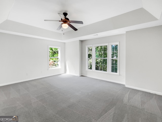 empty room with a raised ceiling, carpet flooring, a wealth of natural light, and ceiling fan