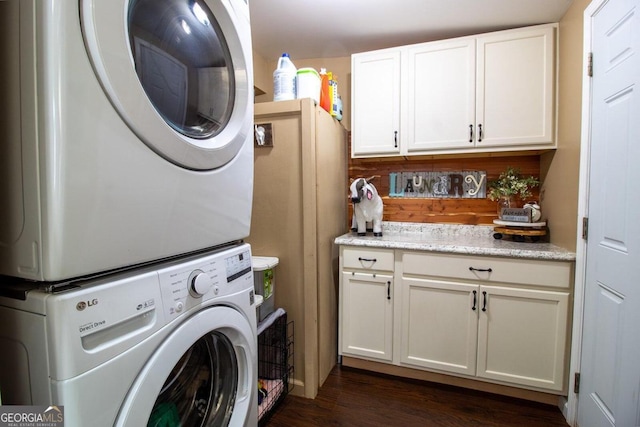 laundry room featuring dark wood-type flooring, stacked washing maching and dryer, and cabinets