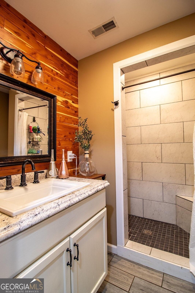 bathroom featuring wooden walls, walk in shower, vanity, and wood-type flooring