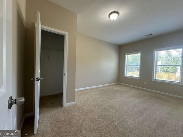 unfurnished bedroom featuring light carpet and a walk in closet