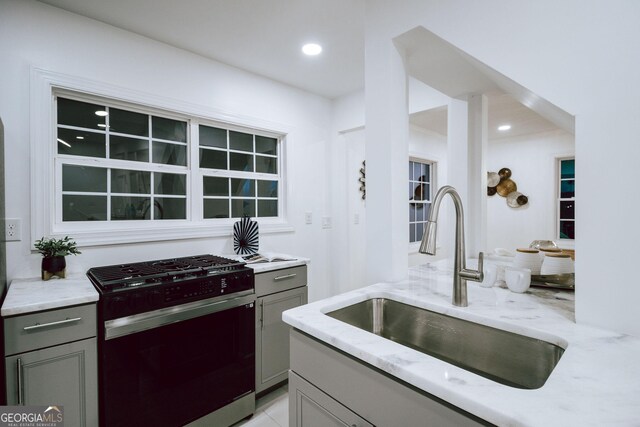 kitchen featuring gray cabinets, light stone countertops, sink, and stainless steel gas range