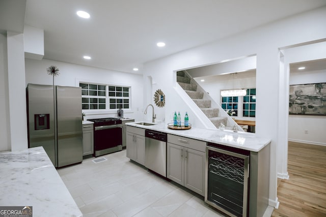 kitchen with light stone countertops, appliances with stainless steel finishes, sink, and beverage cooler