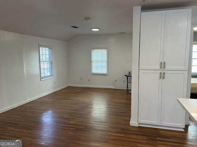 unfurnished bedroom with vaulted ceiling, visible vents, baseboards, and dark wood-style flooring