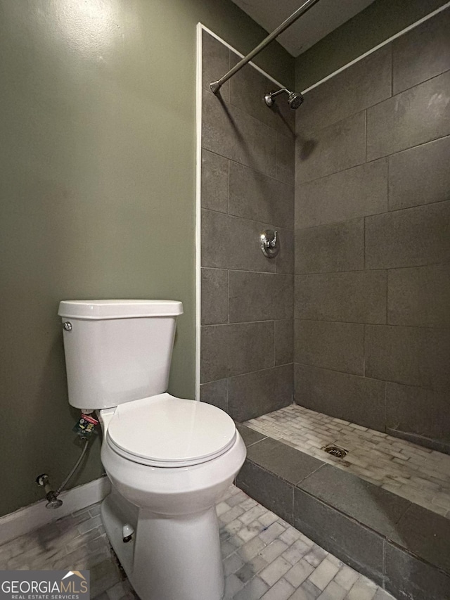 full bath with toilet, baseboards, and tiled shower