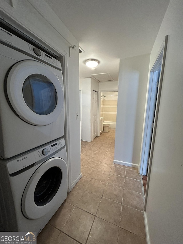 washroom with attic access, stacked washer / dryer, light tile patterned floors, and baseboards