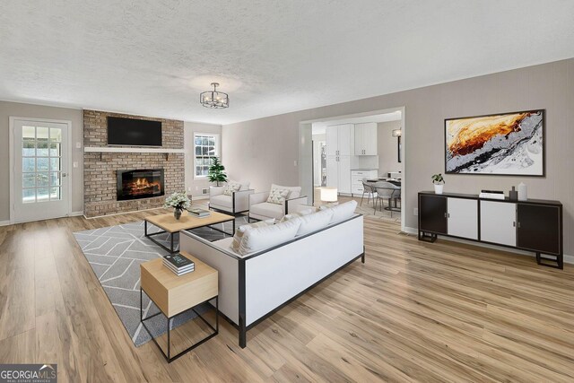 living room with light wood-type flooring, a textured ceiling, a wealth of natural light, and a brick fireplace