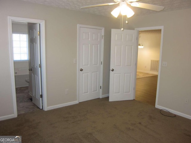 unfurnished bedroom featuring ceiling fan, dark carpet, a textured ceiling, and ensuite bath