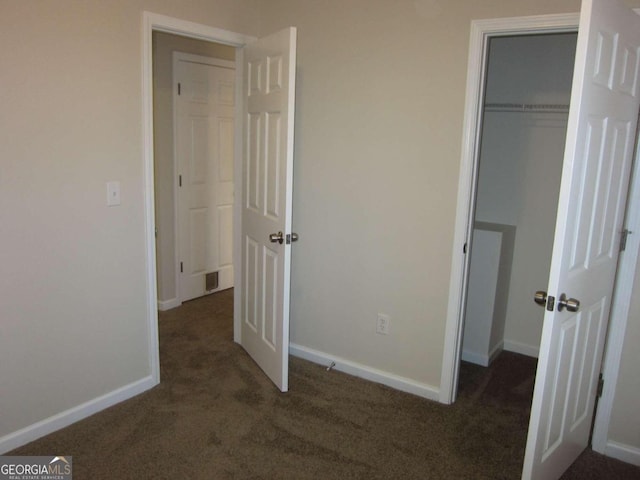 unfurnished bedroom with dark carpet and a closet