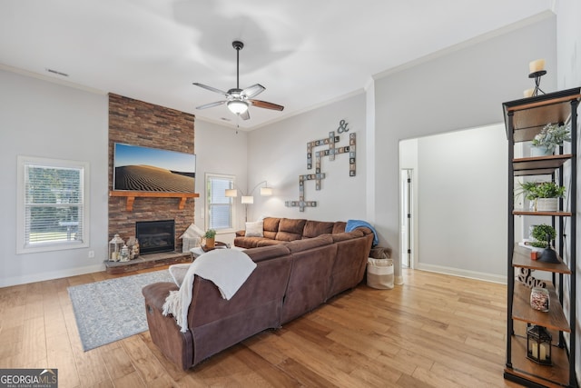 living room featuring ceiling fan, crown molding, light hardwood / wood-style flooring, and a stone fireplace