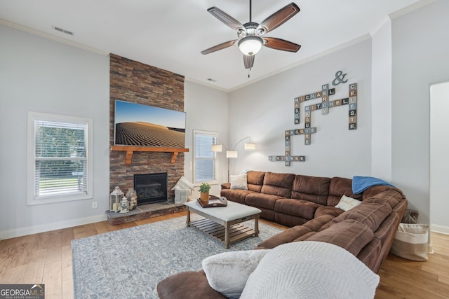 living room featuring wood-type flooring, ceiling fan, crown molding, and a stone fireplace