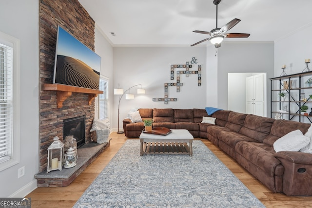 living room with a stone fireplace, crown molding, light hardwood / wood-style floors, and plenty of natural light