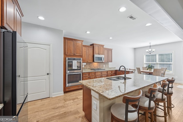 kitchen featuring light wood-type flooring, sink, hanging light fixtures, appliances with stainless steel finishes, and a center island with sink