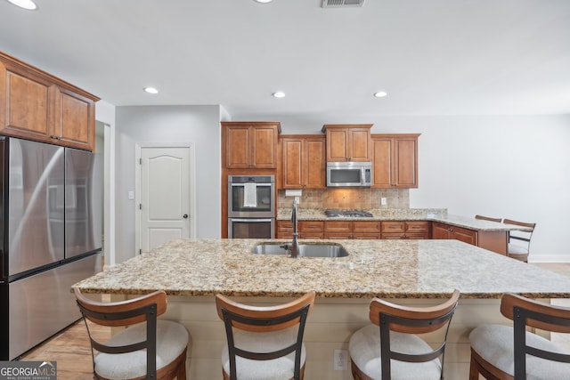 kitchen with light stone counters, sink, appliances with stainless steel finishes, a kitchen breakfast bar, and backsplash