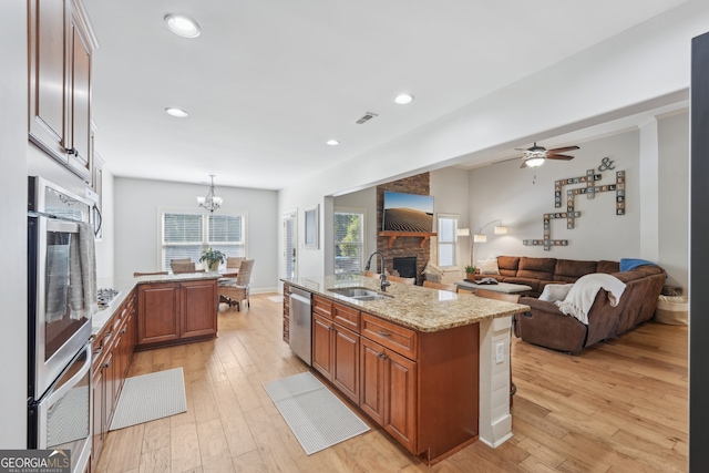 kitchen featuring sink, decorative light fixtures, a center island with sink, stainless steel appliances, and light hardwood / wood-style floors