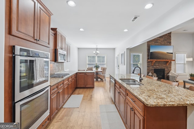 kitchen with sink, light hardwood / wood-style flooring, a chandelier, appliances with stainless steel finishes, and a fireplace