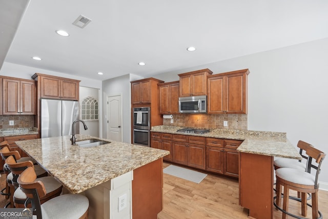 kitchen featuring light wood-type flooring, a kitchen island with sink, sink, appliances with stainless steel finishes, and a kitchen bar