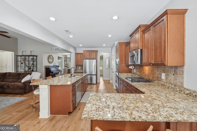 kitchen with appliances with stainless steel finishes, a kitchen bar, light stone counters, and light hardwood / wood-style floors