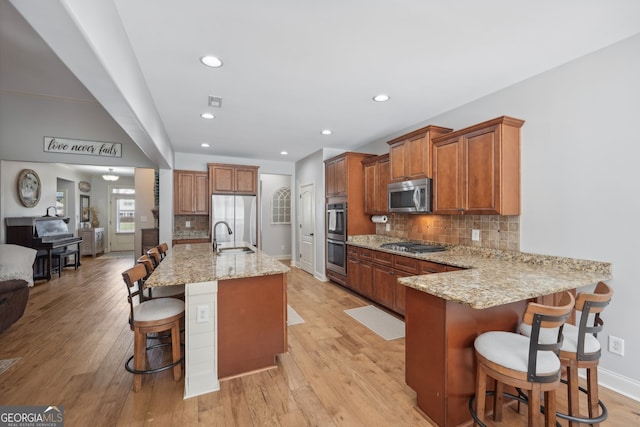 kitchen featuring light wood-type flooring, light stone counters, appliances with stainless steel finishes, a kitchen bar, and backsplash