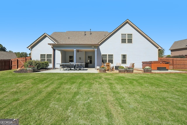 rear view of house featuring ceiling fan, a hot tub, a lawn, and a patio area