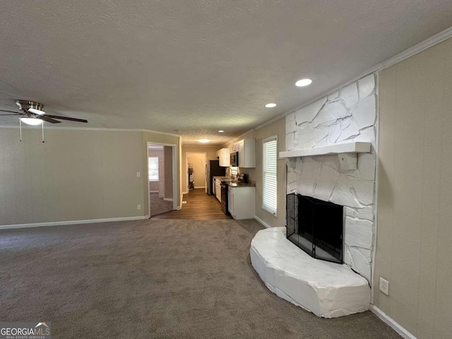 unfurnished living room featuring ceiling fan, a stone fireplace, ornamental molding, and carpet