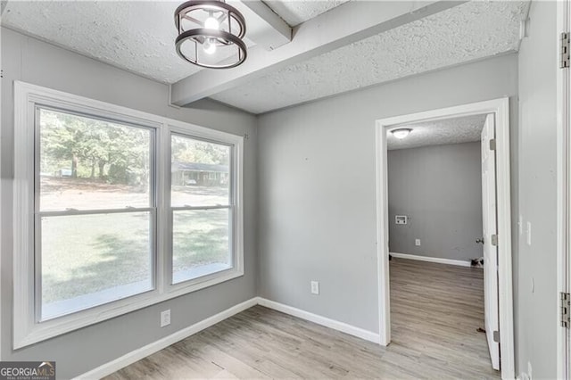 unfurnished room featuring beamed ceiling, light hardwood / wood-style floors, and a textured ceiling