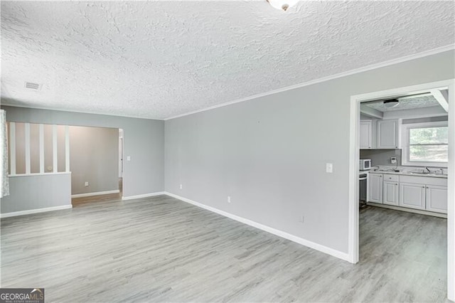 unfurnished living room featuring ornamental molding, light wood-type flooring, sink, and a textured ceiling