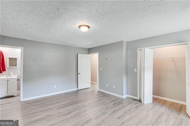 unfurnished bedroom with light wood-type flooring, a closet, connected bathroom, and a textured ceiling