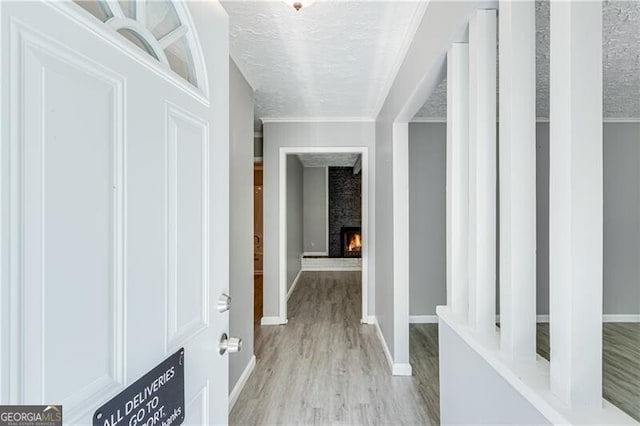 hallway featuring ornamental molding, light hardwood / wood-style floors, and a textured ceiling