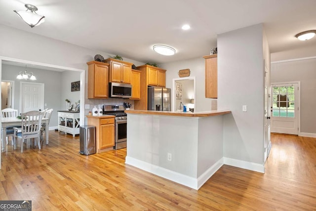 kitchen with kitchen peninsula, light hardwood / wood-style flooring, backsplash, appliances with stainless steel finishes, and an inviting chandelier