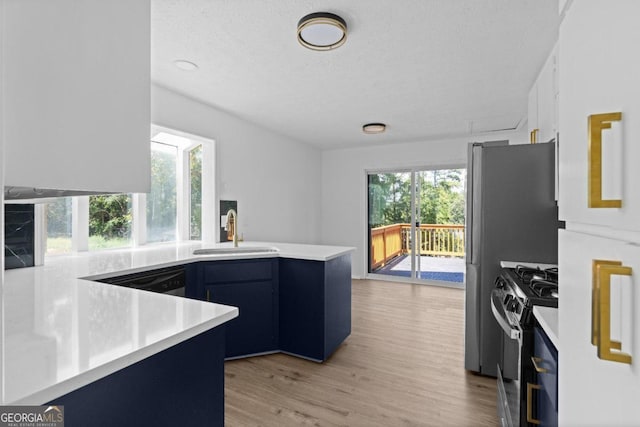 kitchen with blue cabinets, sink, kitchen peninsula, stainless steel appliances, and light wood-type flooring