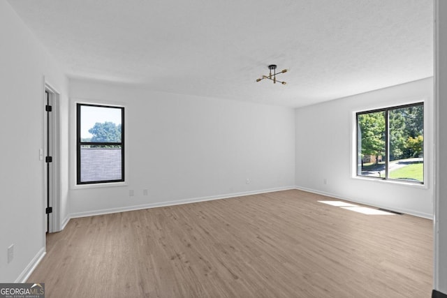 unfurnished room with plenty of natural light, an inviting chandelier, light wood-type flooring, and a textured ceiling