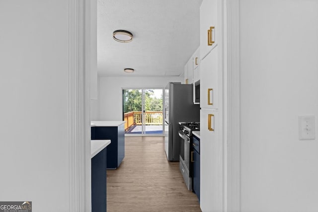 kitchen featuring stainless steel appliances, light hardwood / wood-style floors, a textured ceiling, and white cabinetry