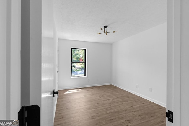 unfurnished room featuring a textured ceiling, dark hardwood / wood-style floors, and a chandelier