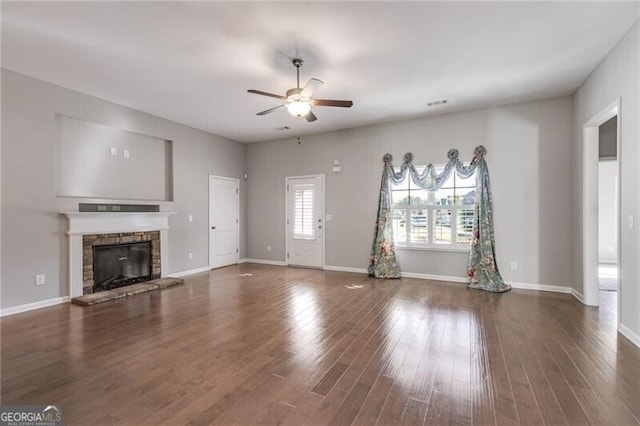 unfurnished living room with dark wood-type flooring, a stone fireplace, and ceiling fan