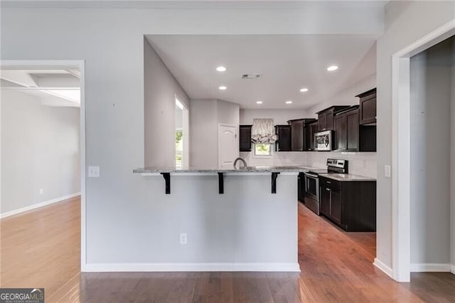 kitchen with tasteful backsplash, light stone countertops, stainless steel appliances, hardwood / wood-style flooring, and a breakfast bar area