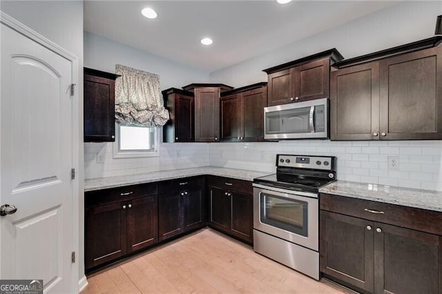 kitchen featuring dark brown cabinets, appliances with stainless steel finishes, light wood-type flooring, and light stone counters