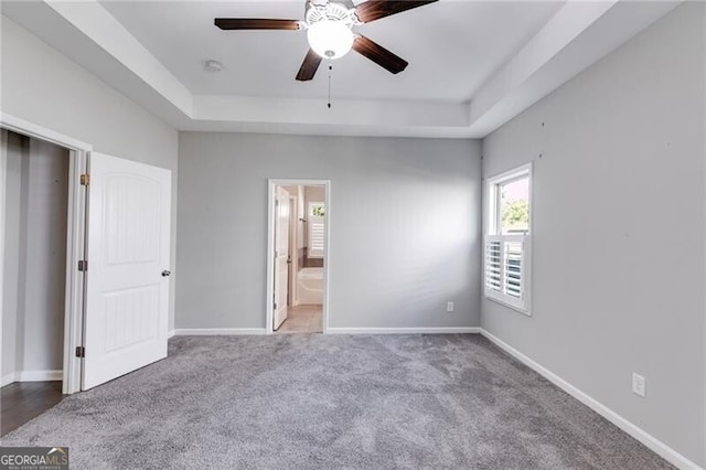 unfurnished bedroom featuring ensuite bath, carpet flooring, a tray ceiling, and ceiling fan