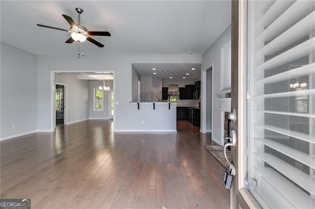 unfurnished living room with ceiling fan with notable chandelier and dark hardwood / wood-style flooring