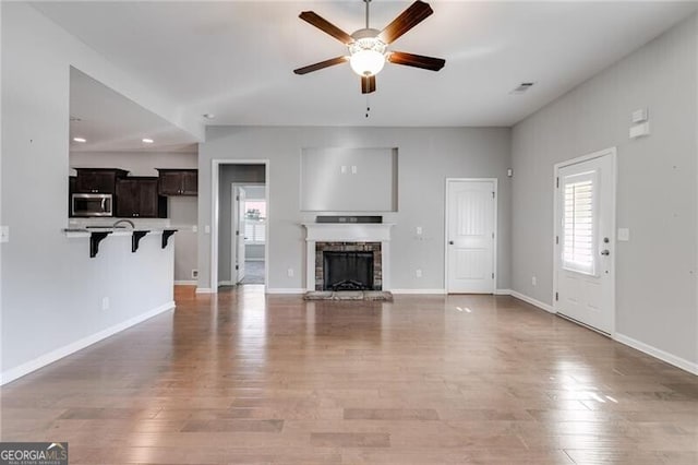 unfurnished living room featuring a stone fireplace, hardwood / wood-style flooring, and ceiling fan