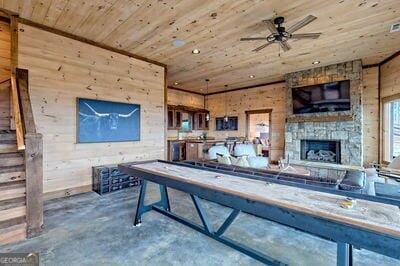 recreation room featuring wooden walls, ceiling fan, wood ceiling, a fireplace, and concrete flooring