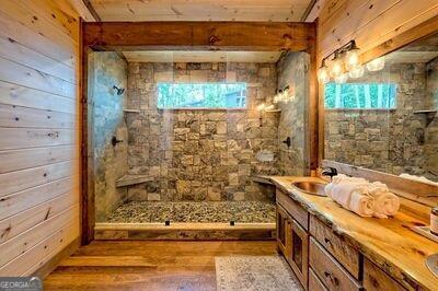 bathroom featuring wood-type flooring, vanity, wooden walls, and tiled shower